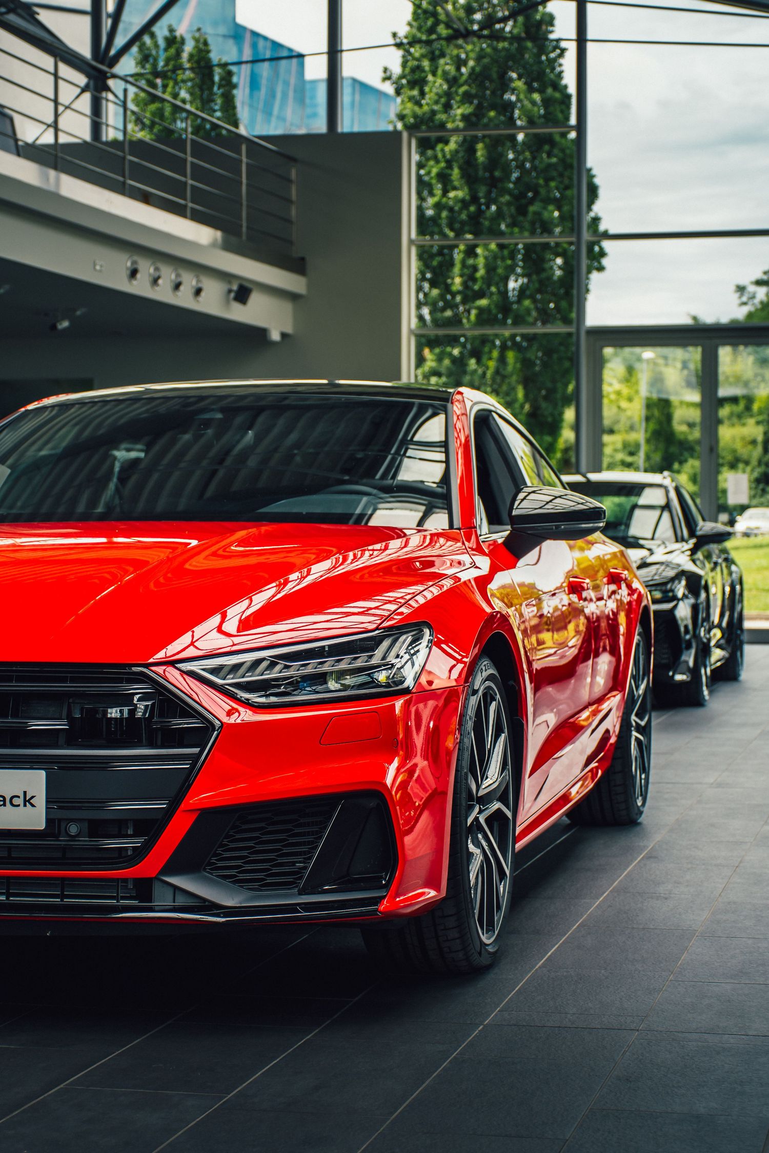 Red Audi S7 Sportback displayed in a modern glass-ceiling dealership showroom with black cars in background.