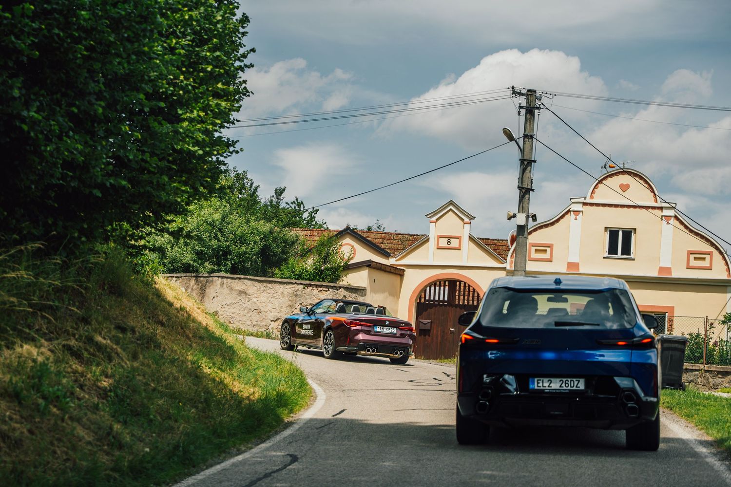 Blue SUV and convertible parked outside a rustic European farmhouse on a rural road.