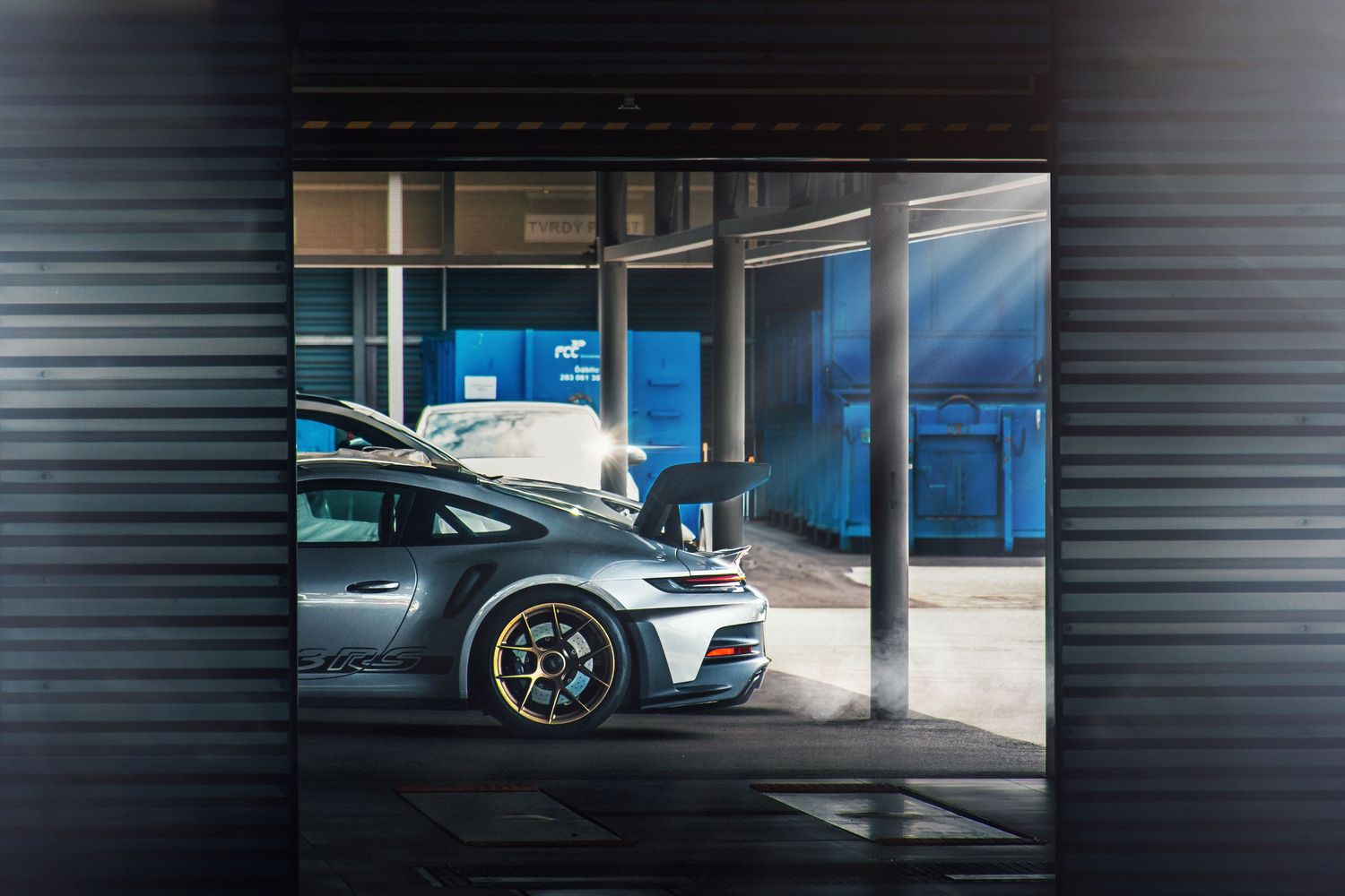 Silver Porsche 911 GT3 RS parked inside a modern garage with dramatic sunlight streaming in.