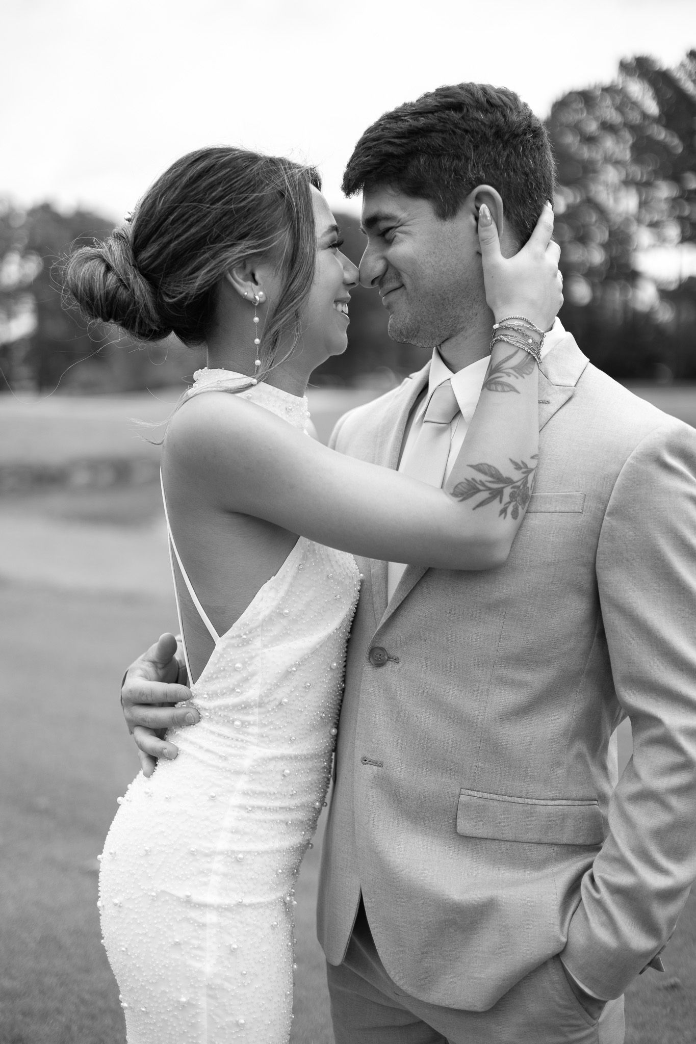 Black and white photo of a bride and groom sharing a romantic moment, smiling at each other outdoors.