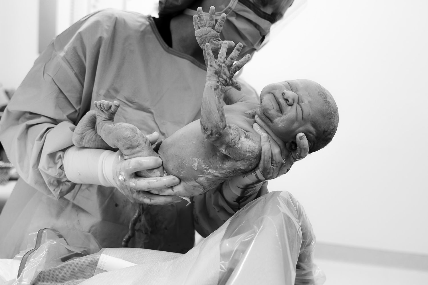 Black and white photo of a medical professional holding a newborn baby immediately after birth in a hospital delivery room.