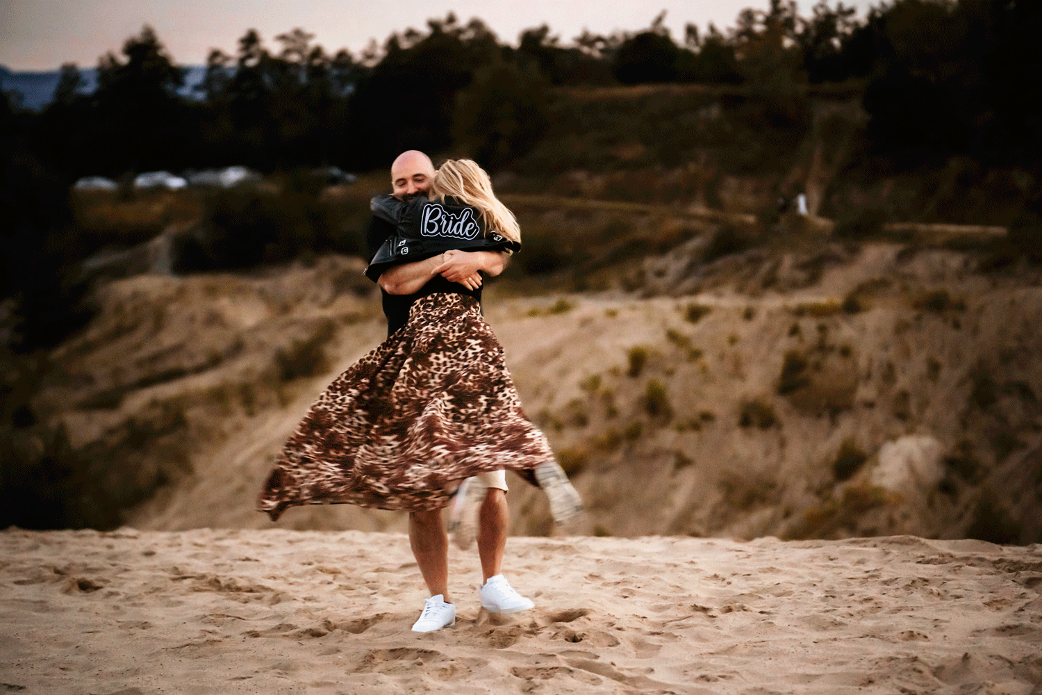 Dancing couple spinning together on sandy terrain at sunset.