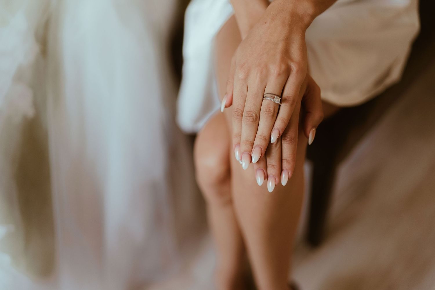 Close-up shot of hands with wedding ring resting on bare leg with soft lighting.