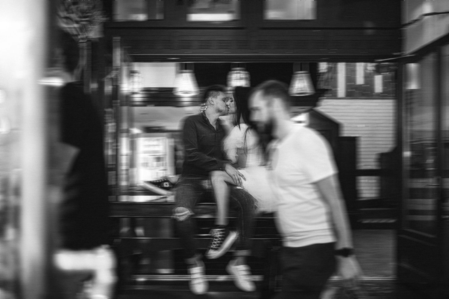 Blurred black and white candid photo outside storefront at night.