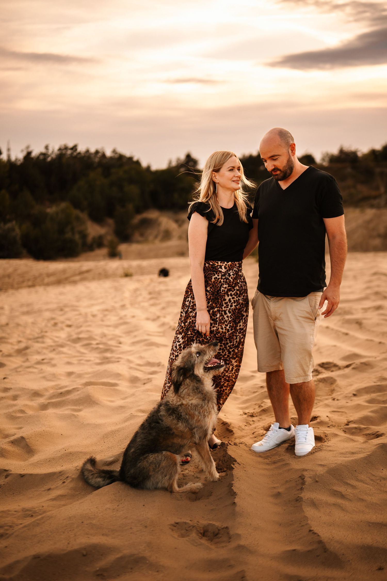 Couple with their dog enjoying sunset moment on desert sand dunes.