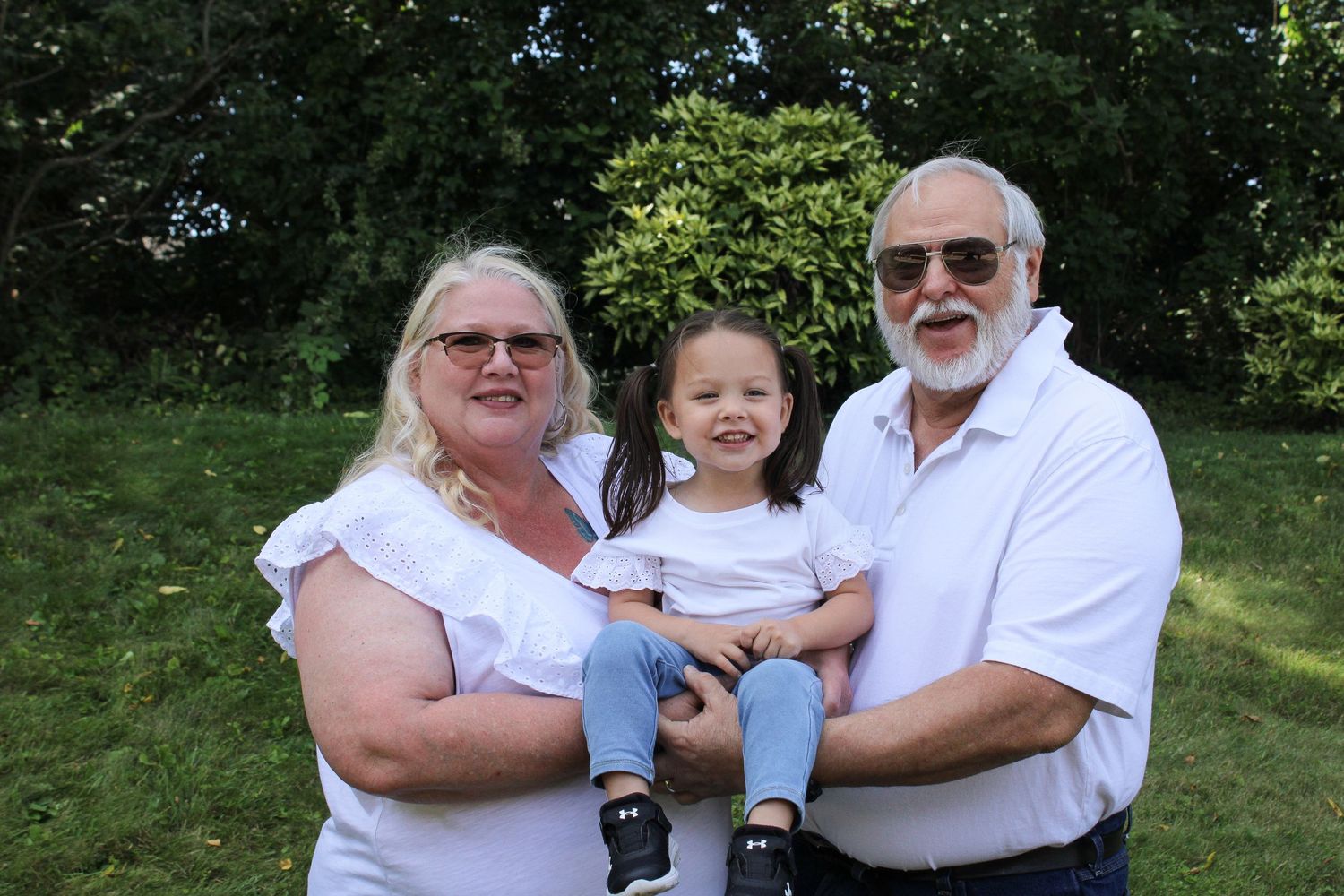 An older man and a woman both dressed in white tee shirts and jeans hold a little girl between them and all three of the