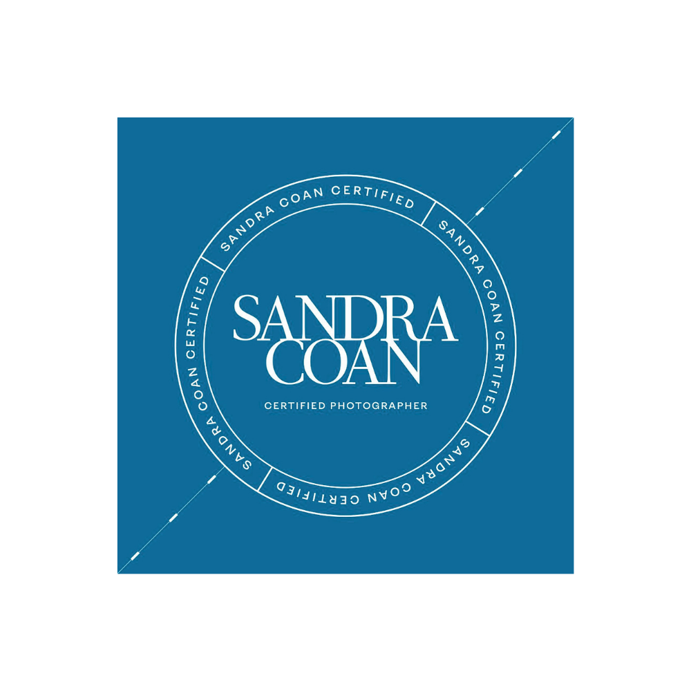 Blue square logo for Sandra Coan Certified Photographer with circular text border and elegant white typography.