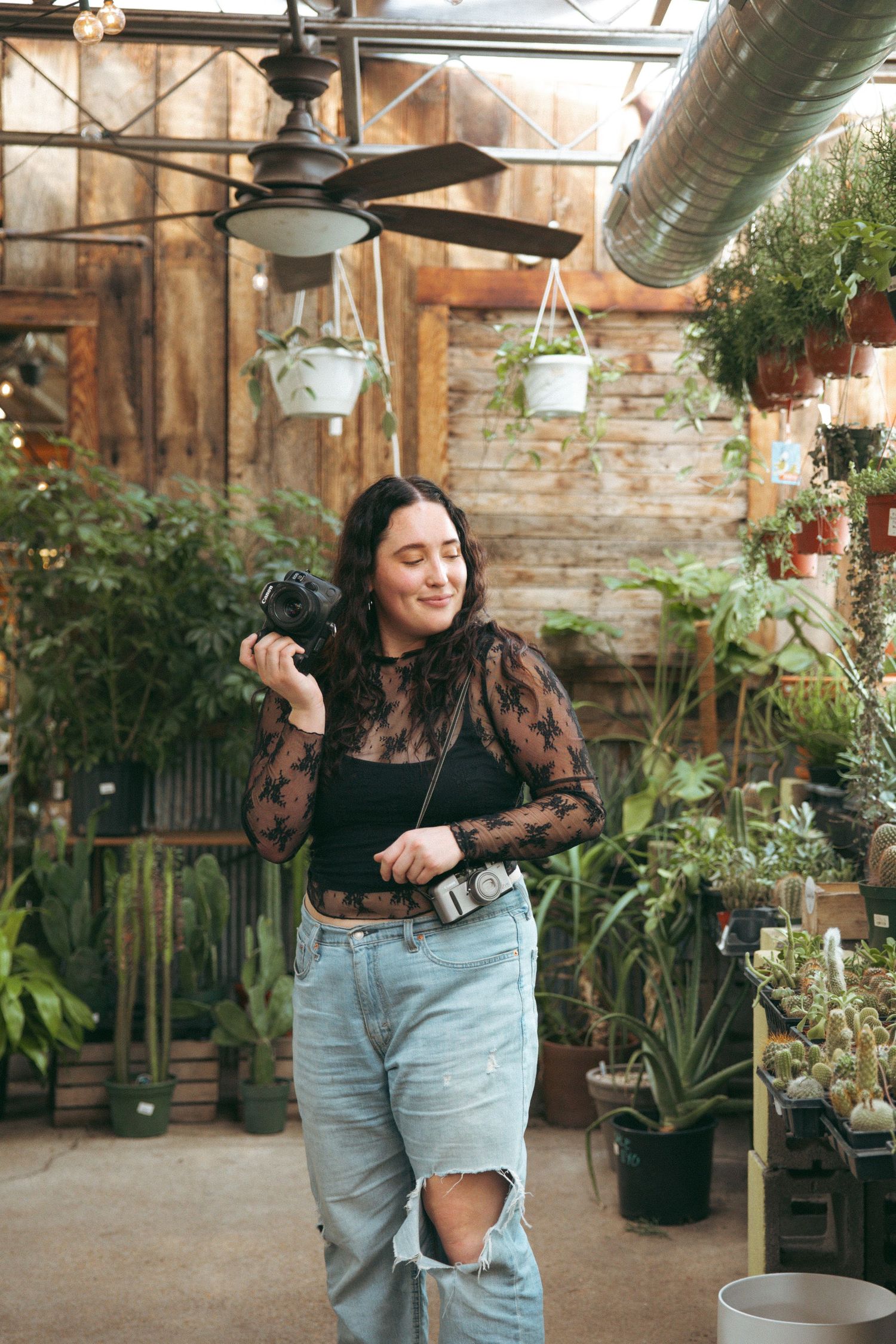 Woman dances joyfully in a greenhouse filled with hanging plants and natural light.