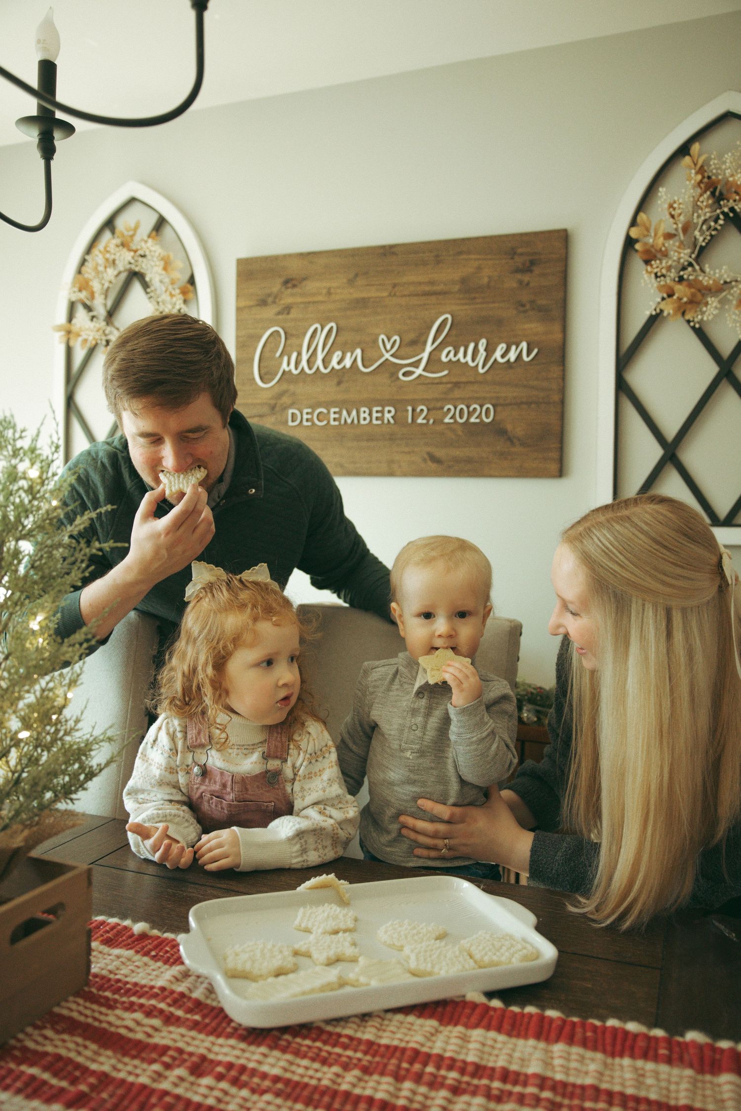 Family enjoys cookies together at a dining table with personalized wedding date sign on wall.