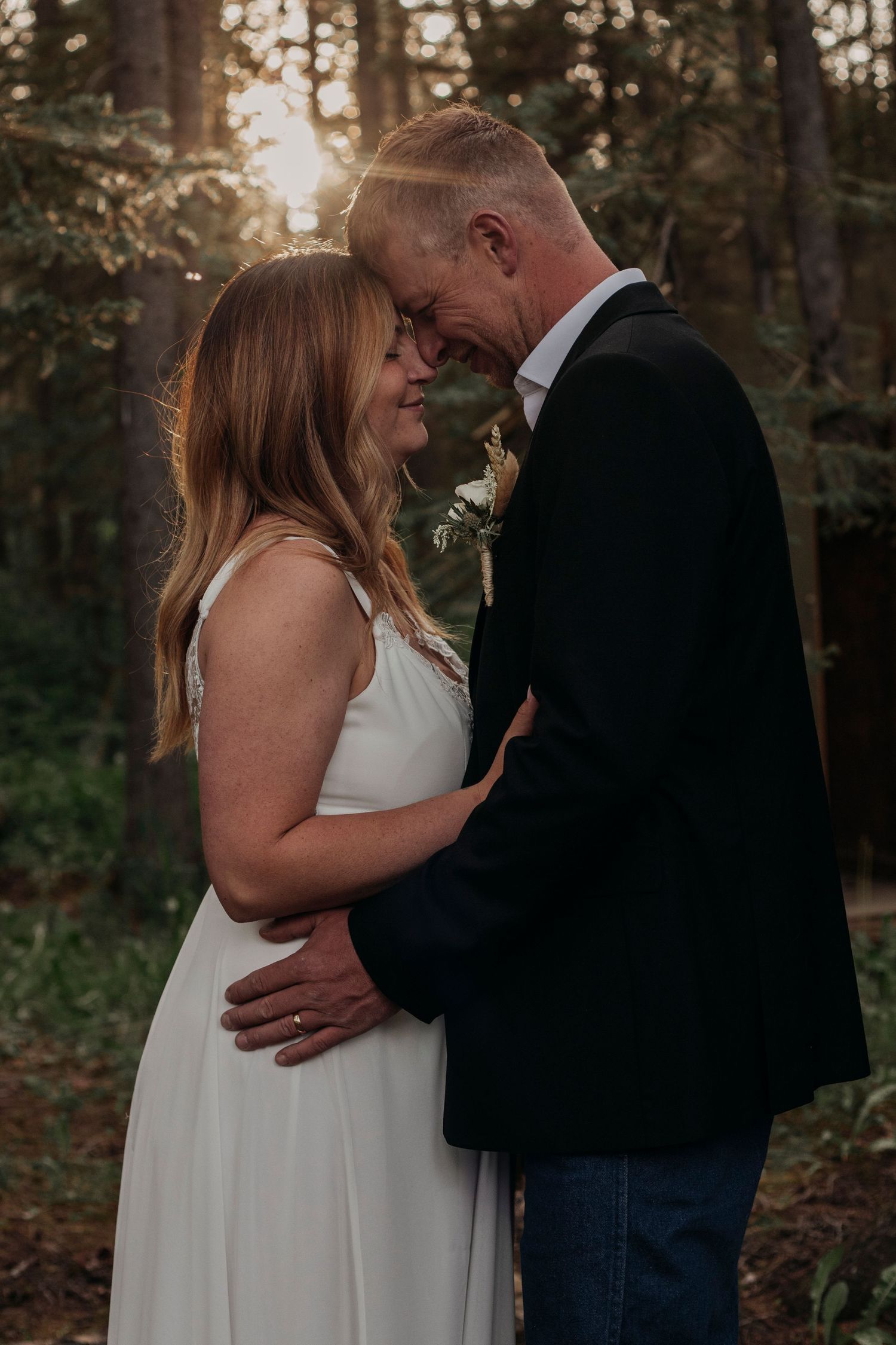 A romantic couple shares an intimate moment in a forest at sunset, with golden light filtering through the trees.