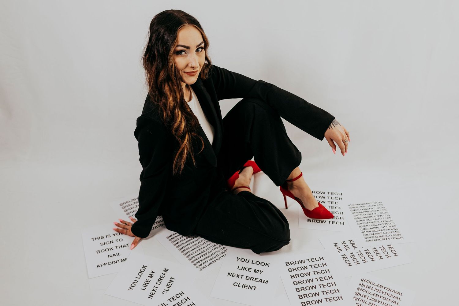 A person in a black blazer sits at a desk writing on multiple papers spread across a white surface.