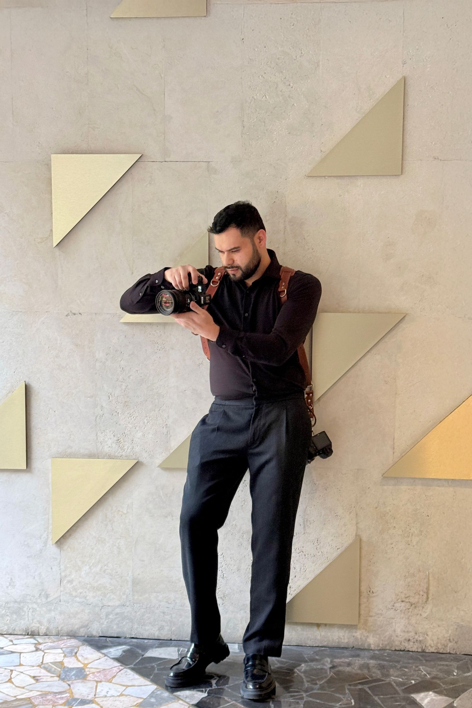 A photographer in dark clothing crouches to take photos against a white wall with geometric paper decorations.