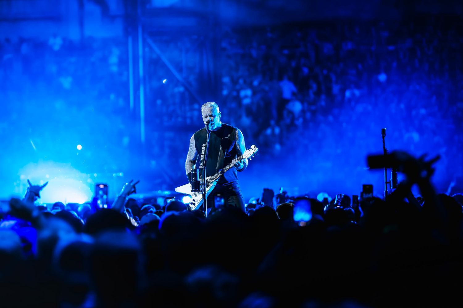 Rock guitarist performing on stage bathed in blue light before a massive crowd at a live concert.