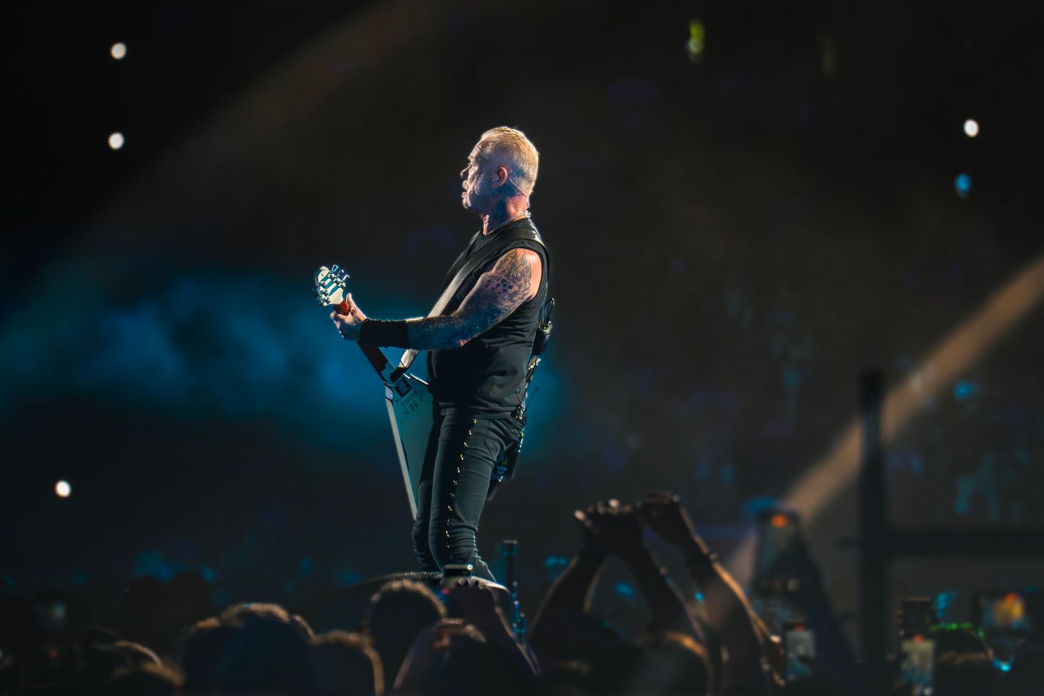 Rock guitarist performs on stage with dramatic lighting and crowd silhouettes at a live concert.