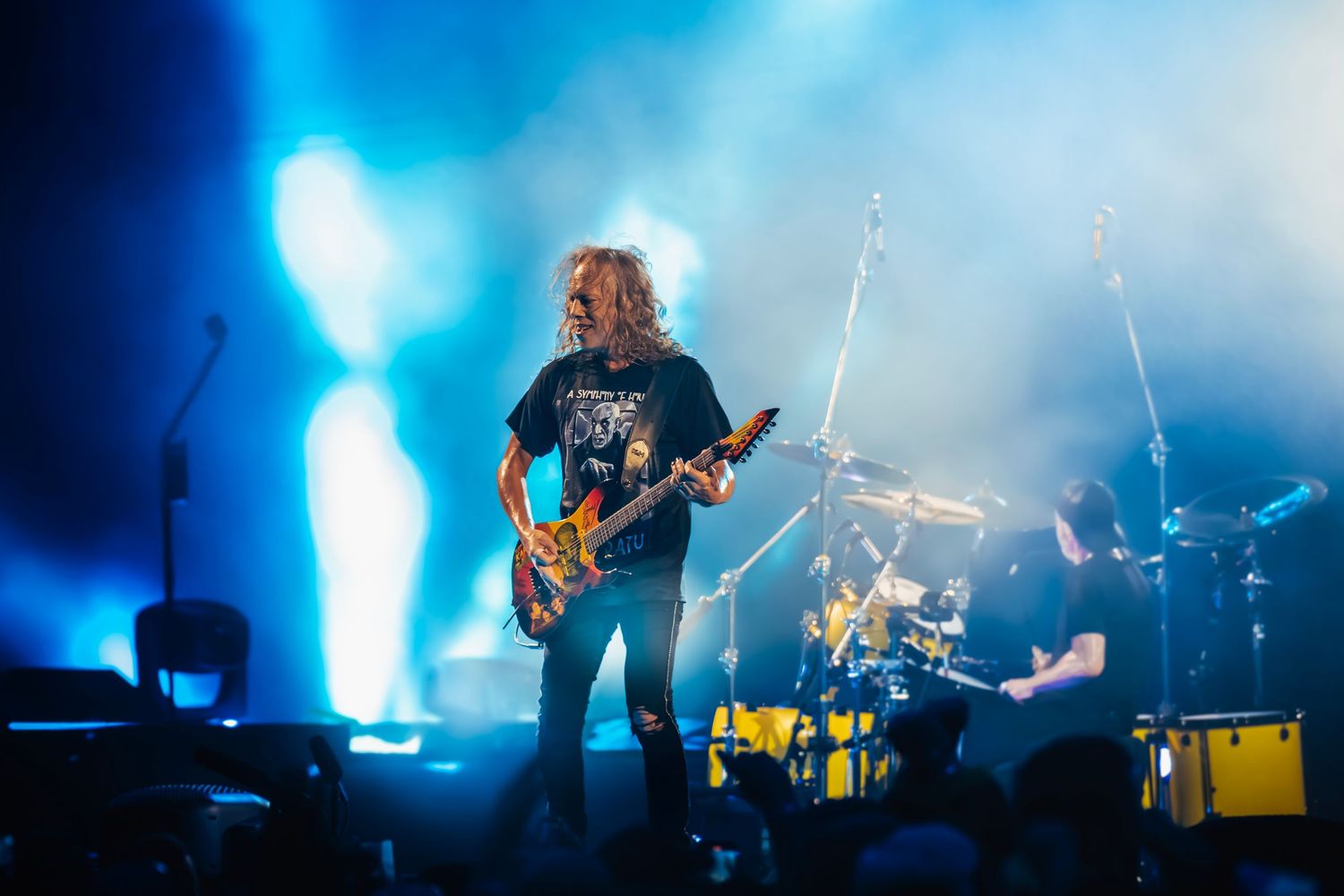 A rock musician performing on stage with a guitar and surrounded by stage lights and smoke.