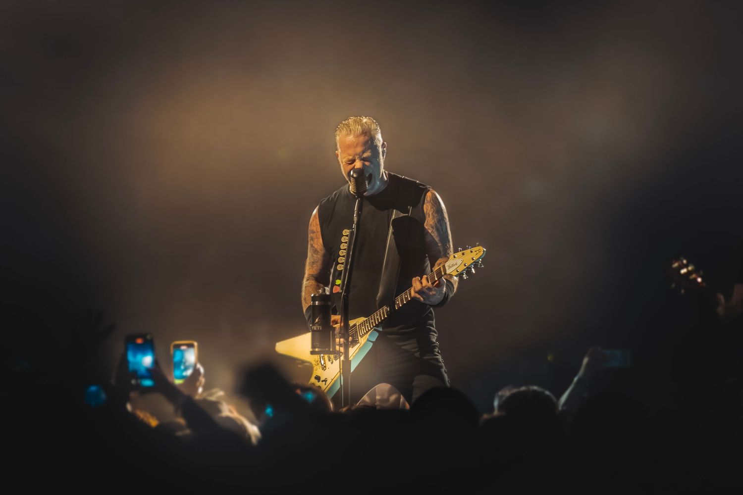 Rock guitarist performing on stage under dramatic fog lights before a large crowd.