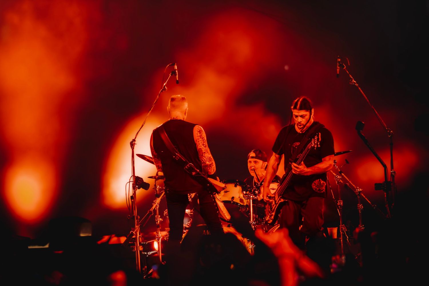 Two guitarists perform on a dramatic red-lit stage with smoke and atmospheric lighting at a rock concert.