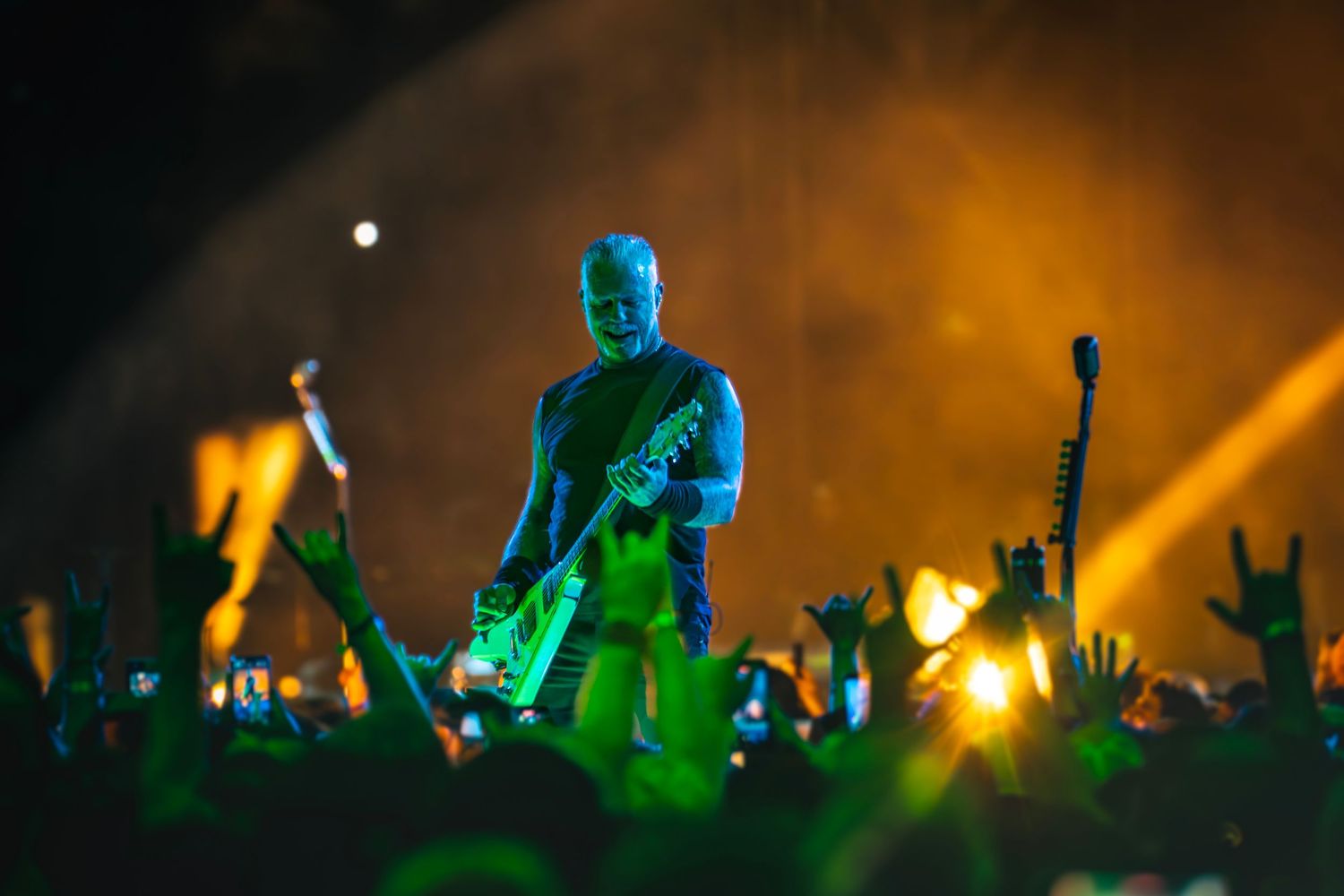 Guitarist performing on stage with green lighting and crowd silhouettes at a live rock concert.
