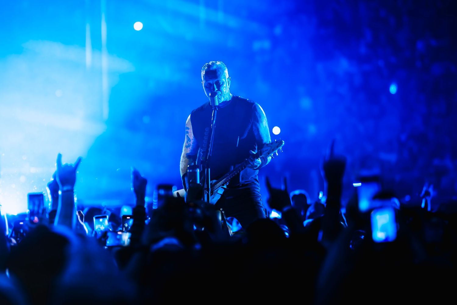 Guitarist performs on stage bathed in blue light before a massive crowd at a live rock concert.