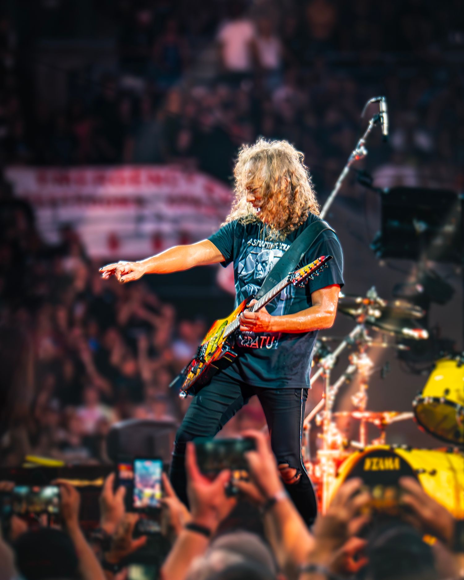 Electric guitarist performs energetically on stage before a massive crowd at a live rock concert under bright lights.