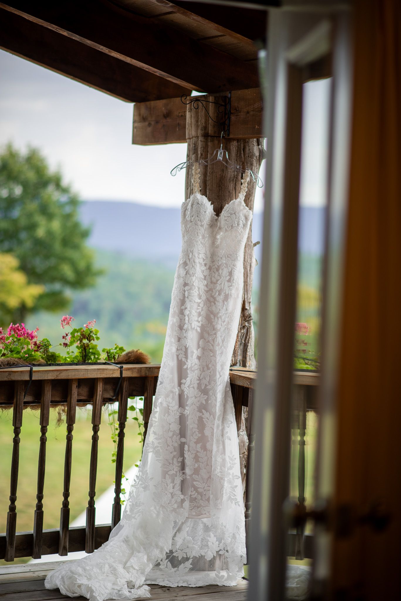 Elegant lace wedding dress hanging on rustic porch with scenic mountain and garden view.