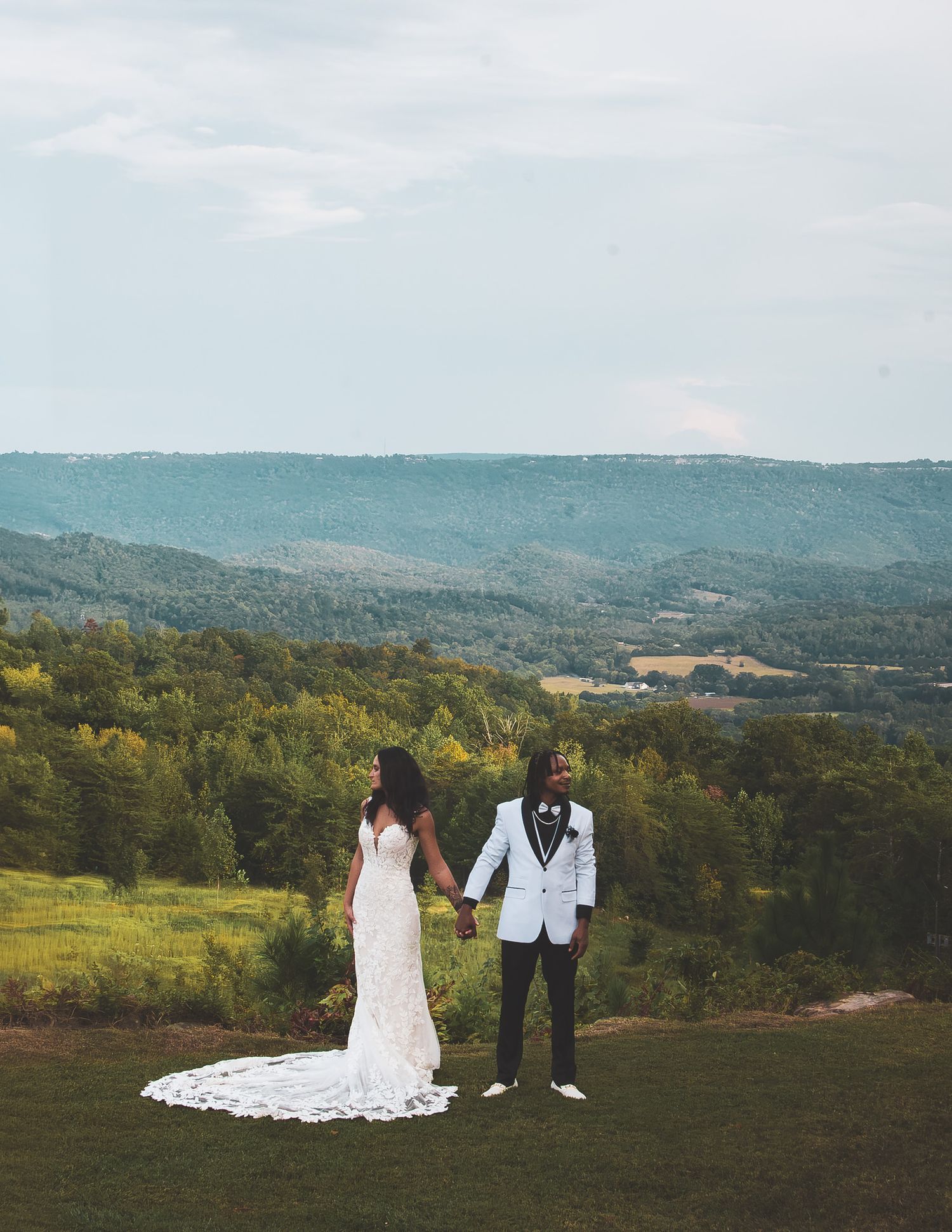 Bride and groom hold hands overlooking a stunning mountain valley landscape on their wedding day.