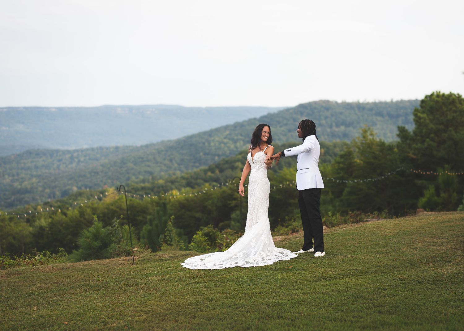 Bride and groom share a tender moment on a hilltop with scenic mountain views behind them.