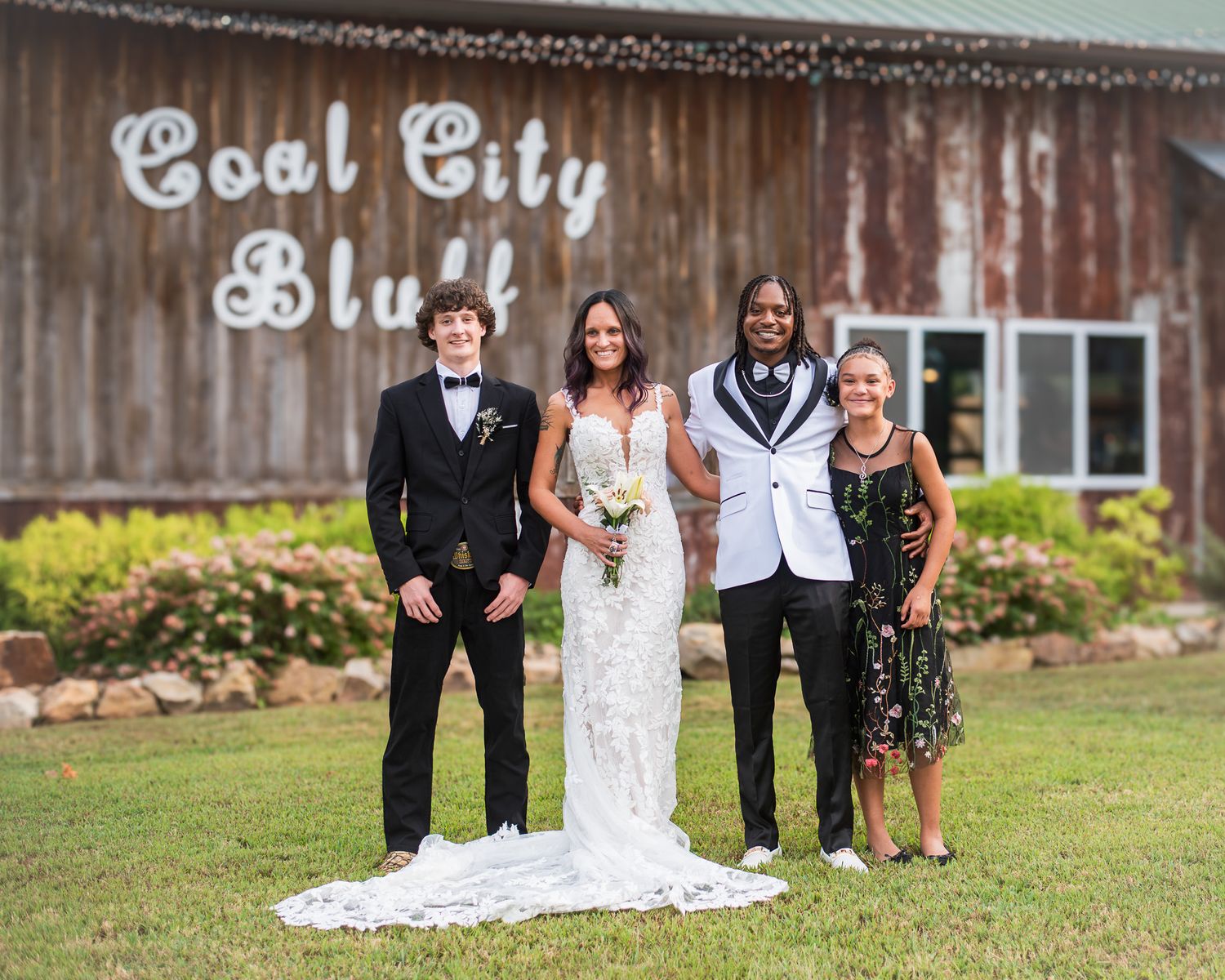 Wedding party poses in front of Coal City Bluff barn venue on a sunny day.