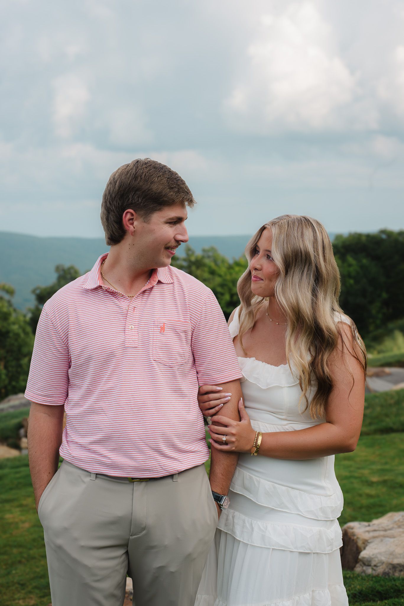 Couple walks arm in arm smiling at each other with mountain landscape in the background.