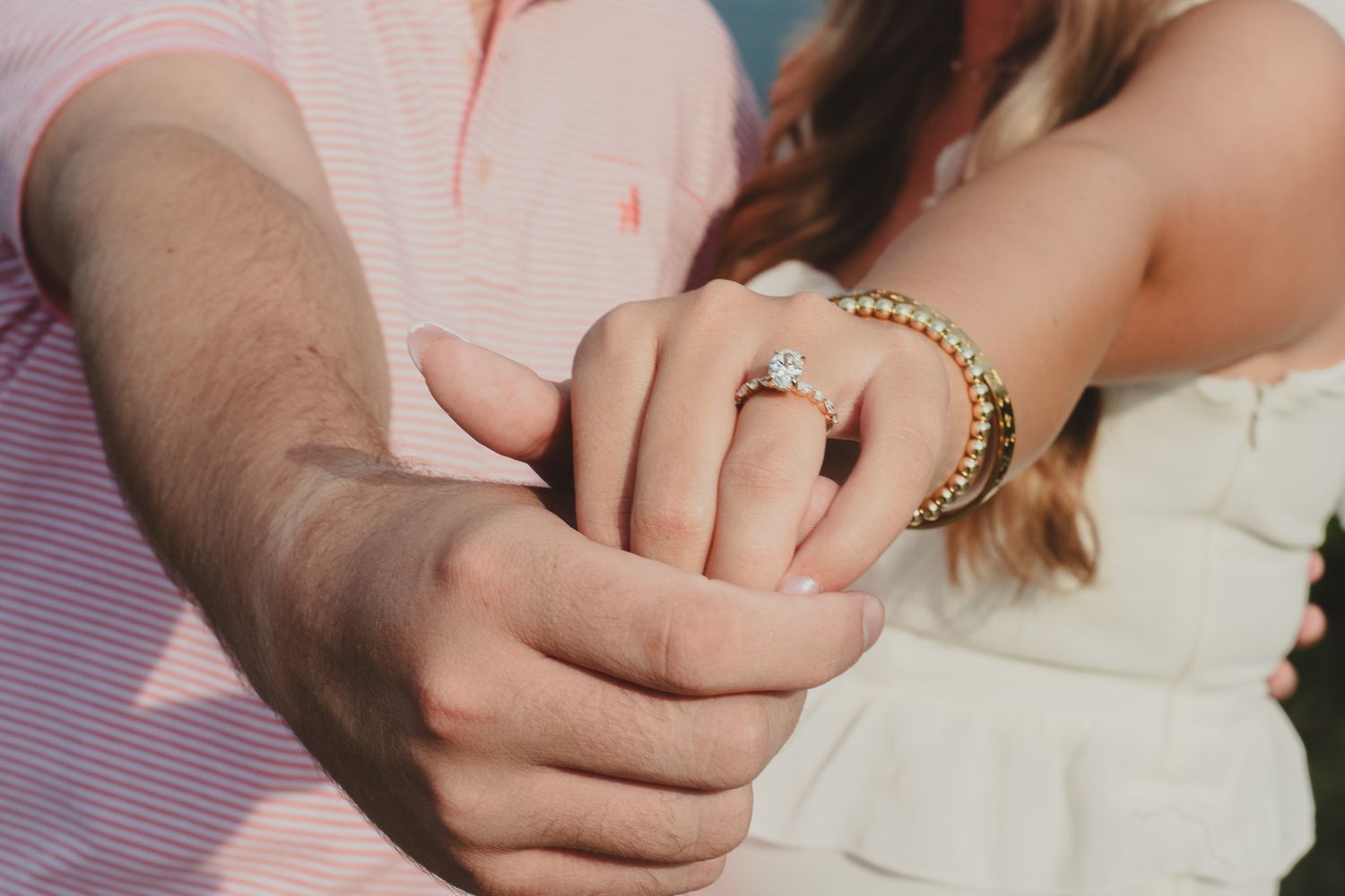 Close-up of engaged couples hands showing sparkling diamond engagement ring and gold beaded bracelet.