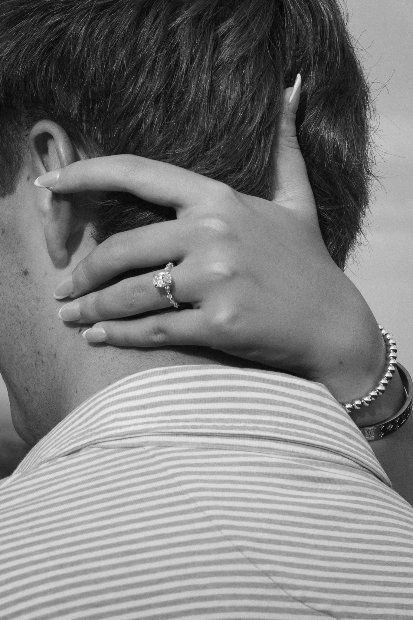 Black and white close-up of womans hand with diamond engagement ring resting on mans neck.