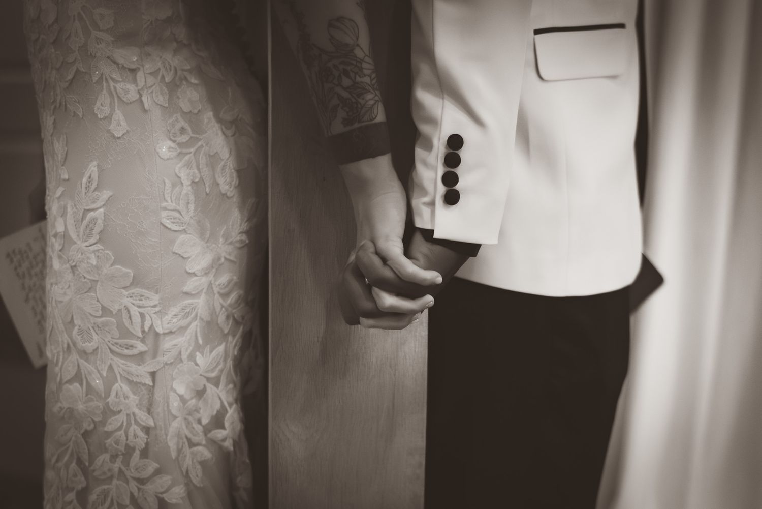 Black and white close-up of bride and groom holding hands in wedding attire.
