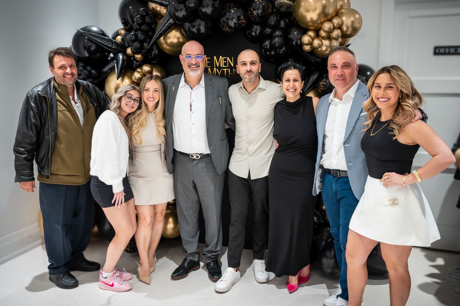 Party attendees gathered for group photos in front of decorative black and gold balloon display.