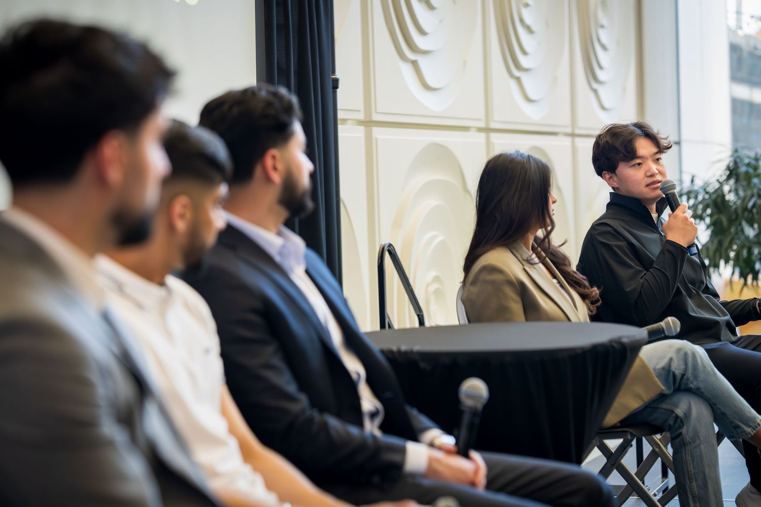 Wide shot of conference panel discussion with speakers seated in front of decorative wall.