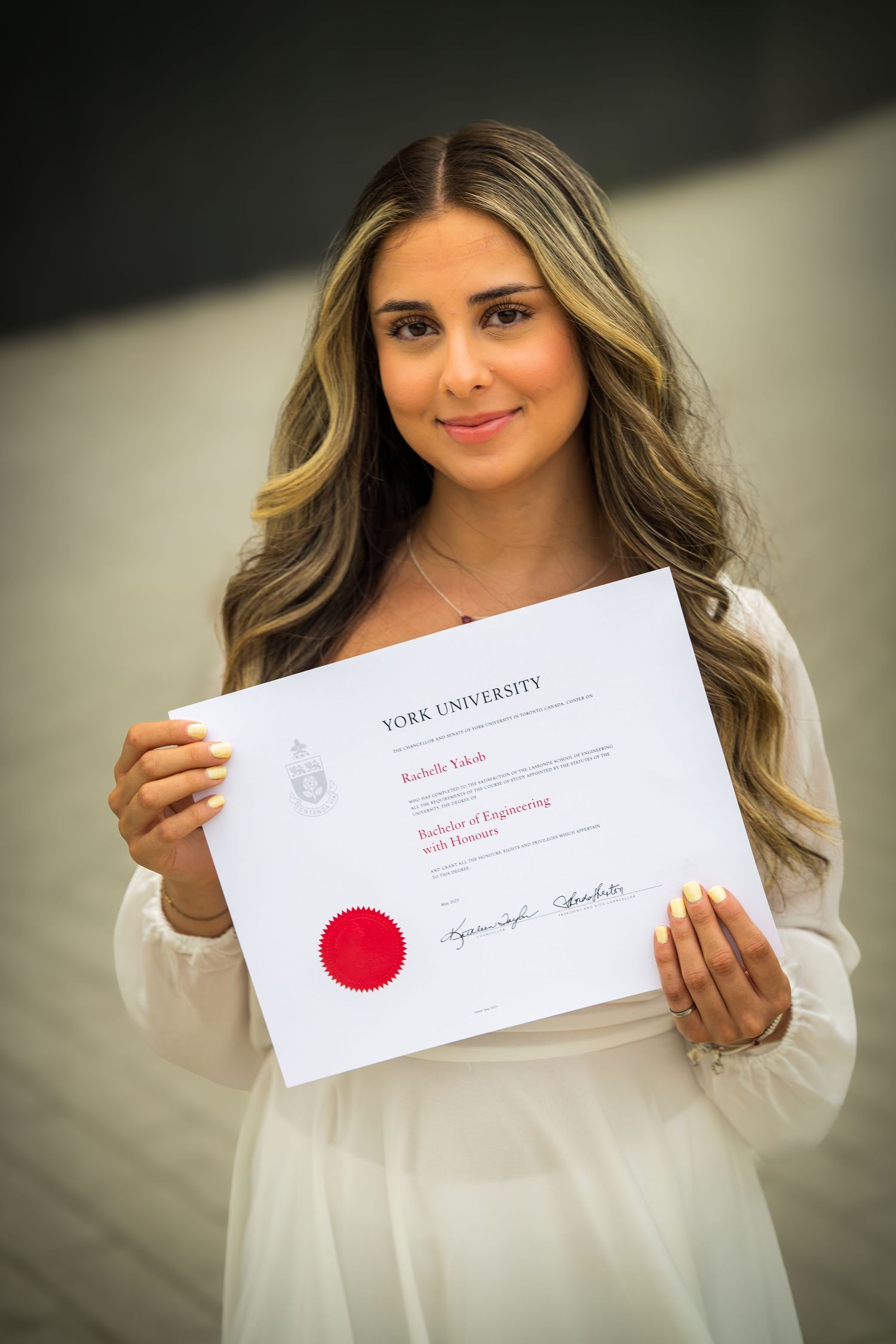 Close-up portrait of graduate displaying York University diploma with bright smile.
