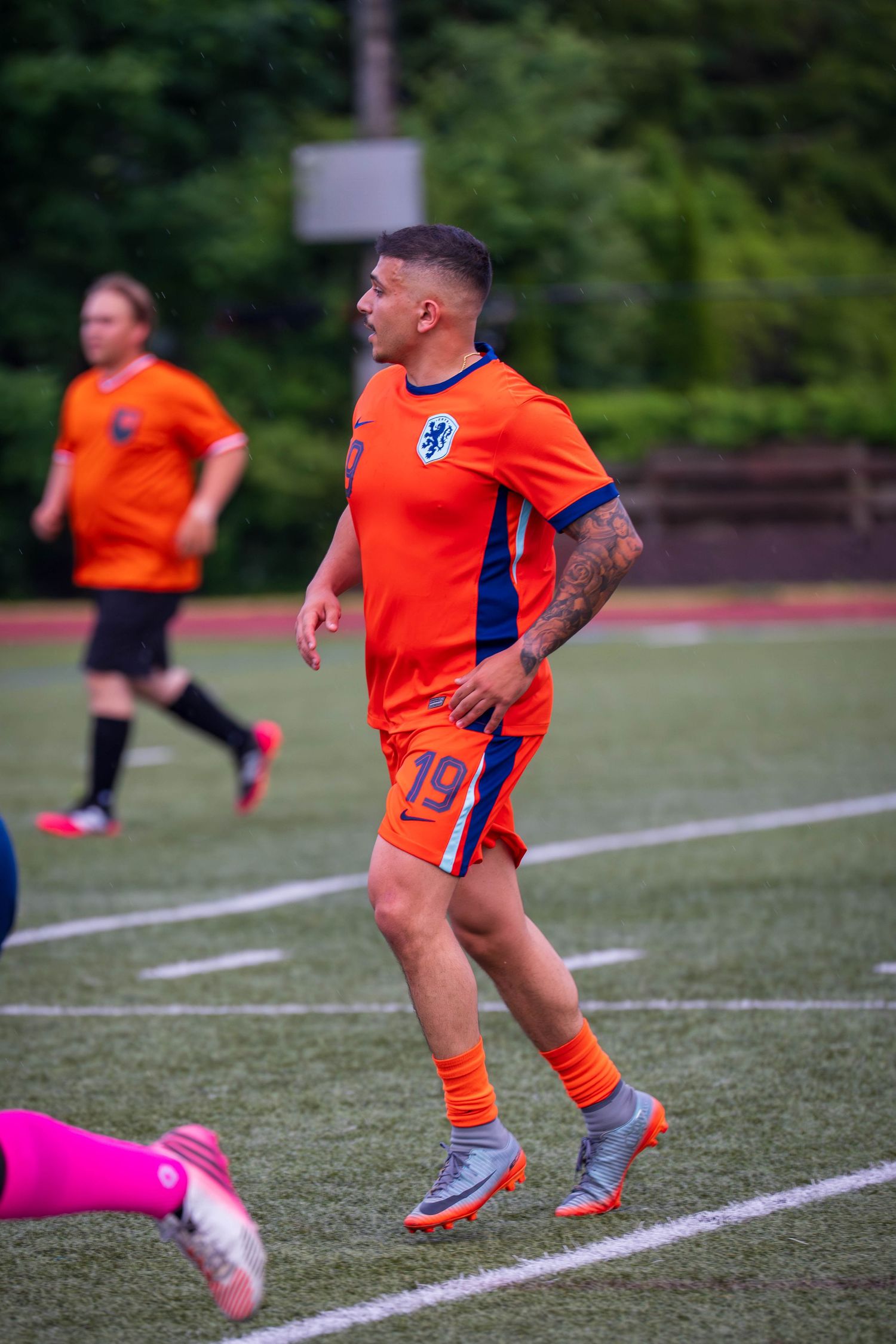 Soccer player in orange jersey performing footwork drills on athletic field.