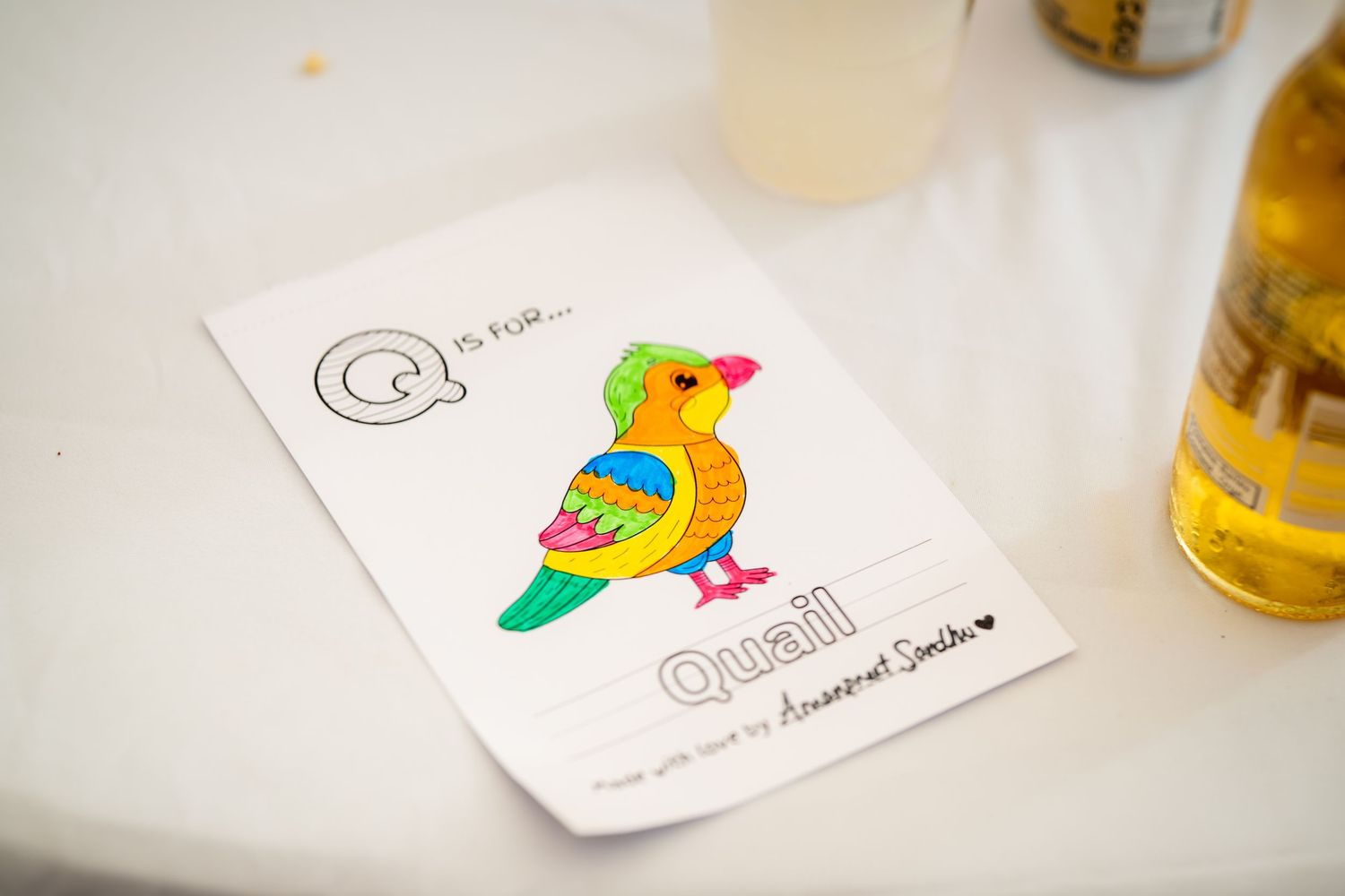 A colorful parrot illustration card sits on a white table next to a bottle.