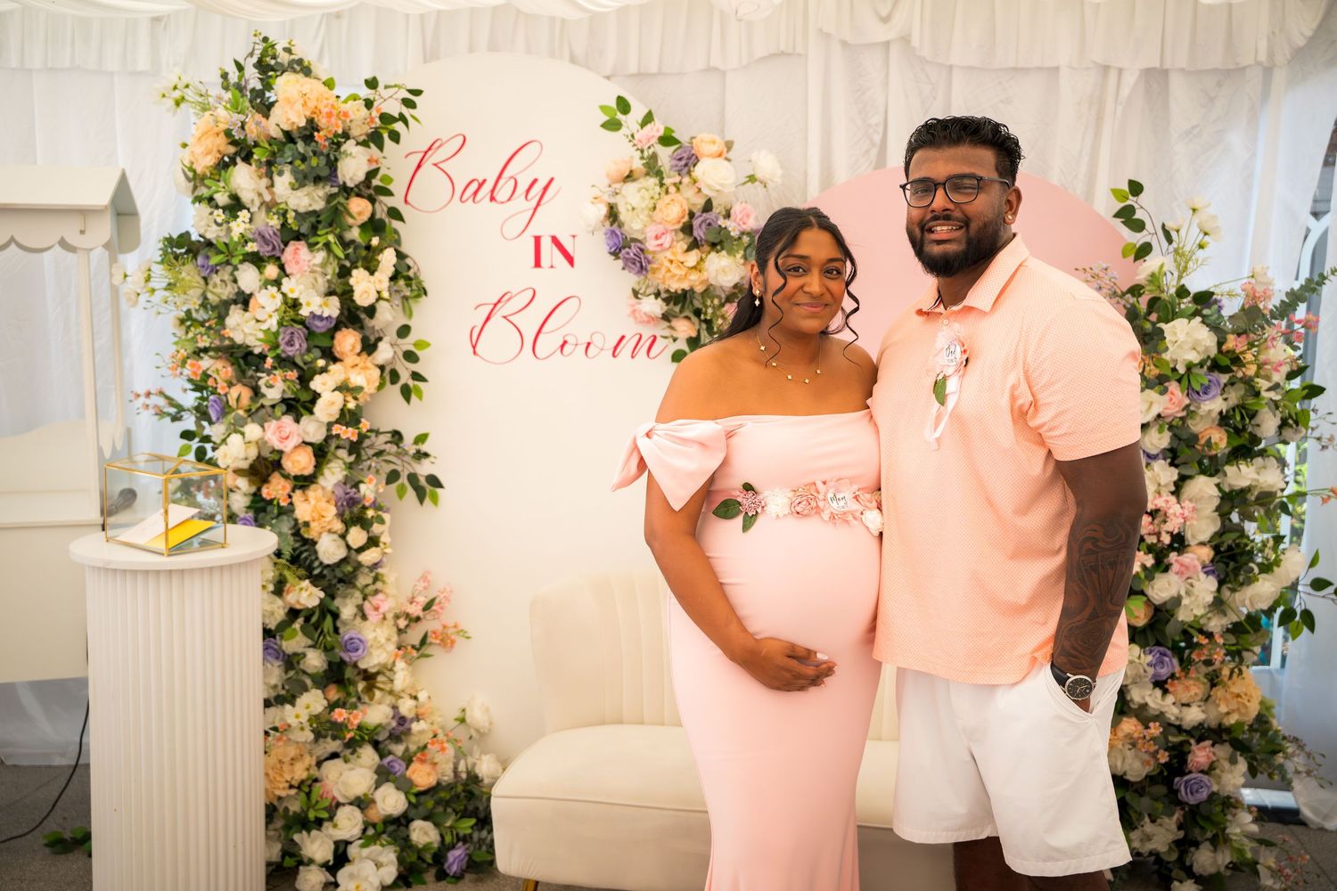 Baby shower celebration with pink theme and floral decorations against white backdrop.