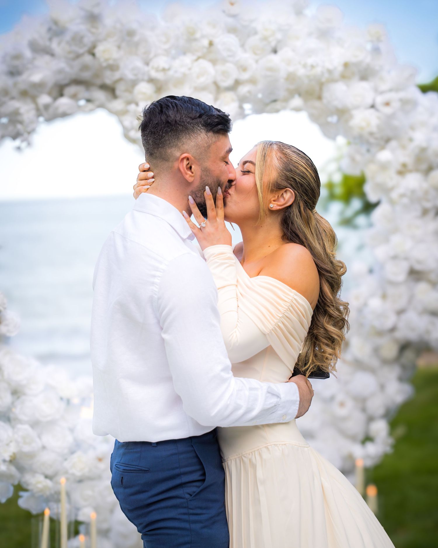Sunset proposal moment under elegant white balloon arch with ocean backdrop.