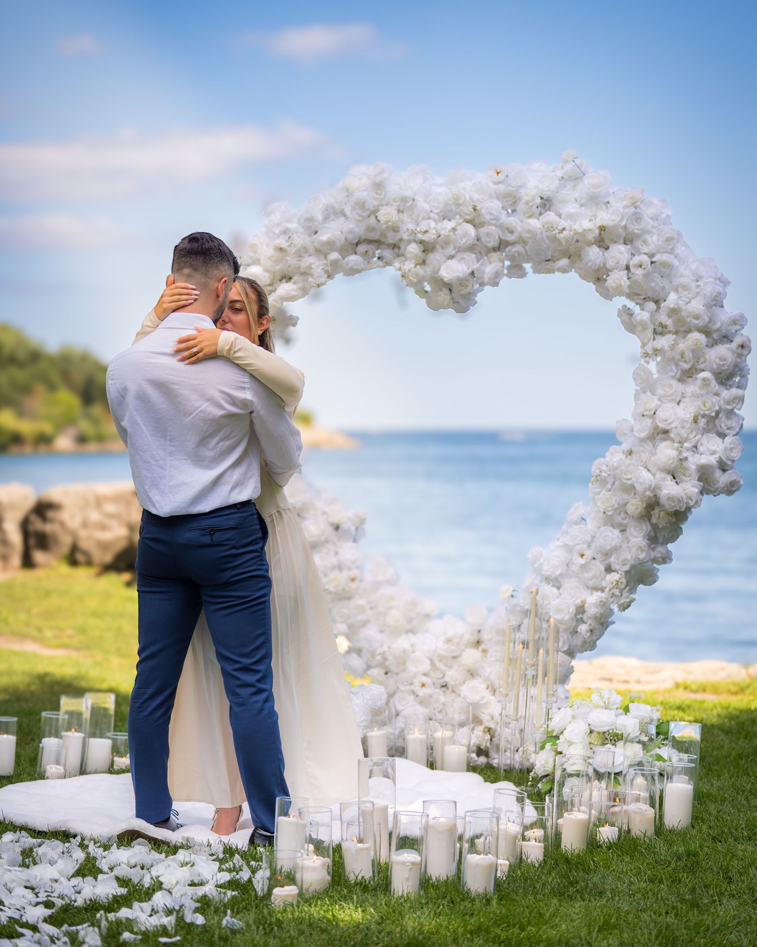 Seaside wedding setup with white floral arch and glowing candles at sunset.