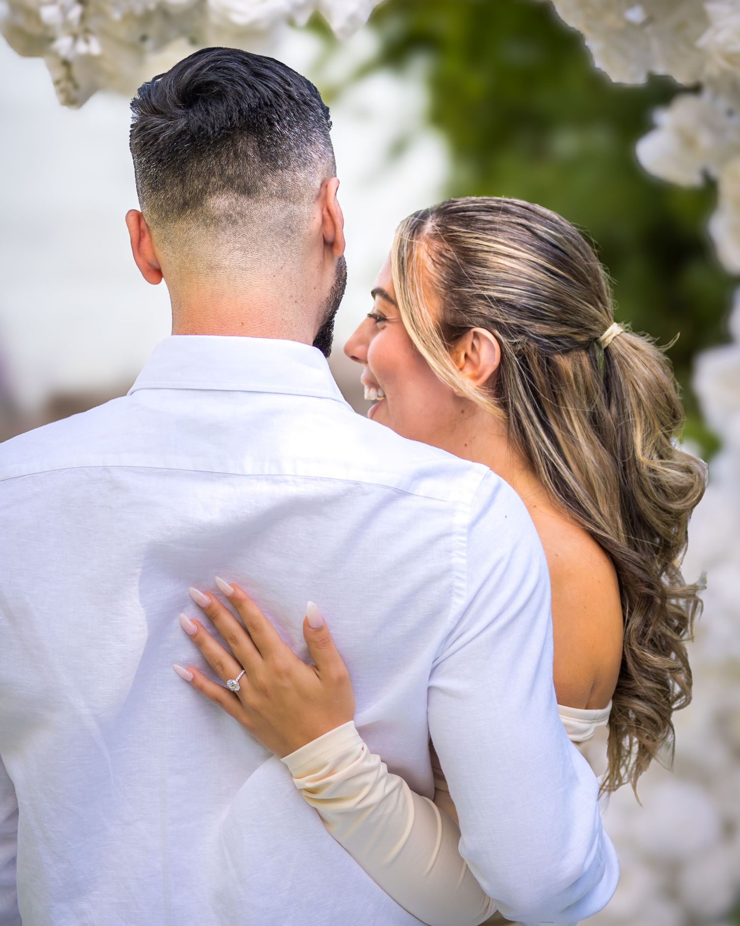 Intimate moment captured between newlyweds under white floral decorations.