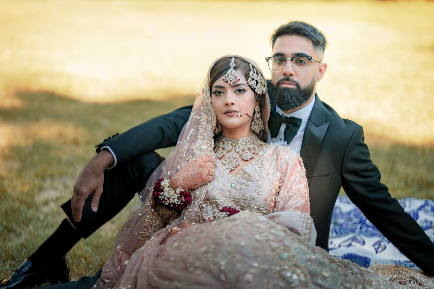 Romantic South Asian wedding portrait with couple seated on blanket during golden hour.