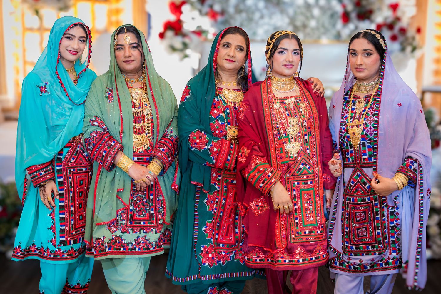 Group of women wearing vibrant traditional South Asian dresses in blue, red, and purple with embroidery.