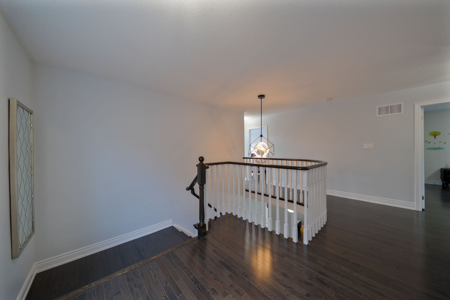 Interior view of empty room with dark hardwood floors and white walls showing partial staircase and doorway.