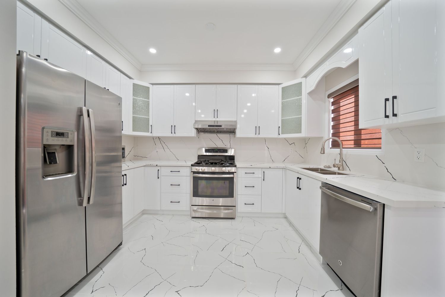 Modern white U-shaped kitchen with stainless steel appliances, marble floors and quartz countertops.