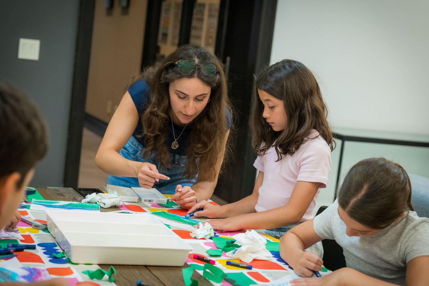 A teacher guides children through a hands-on colorful art and craft activity indoors.