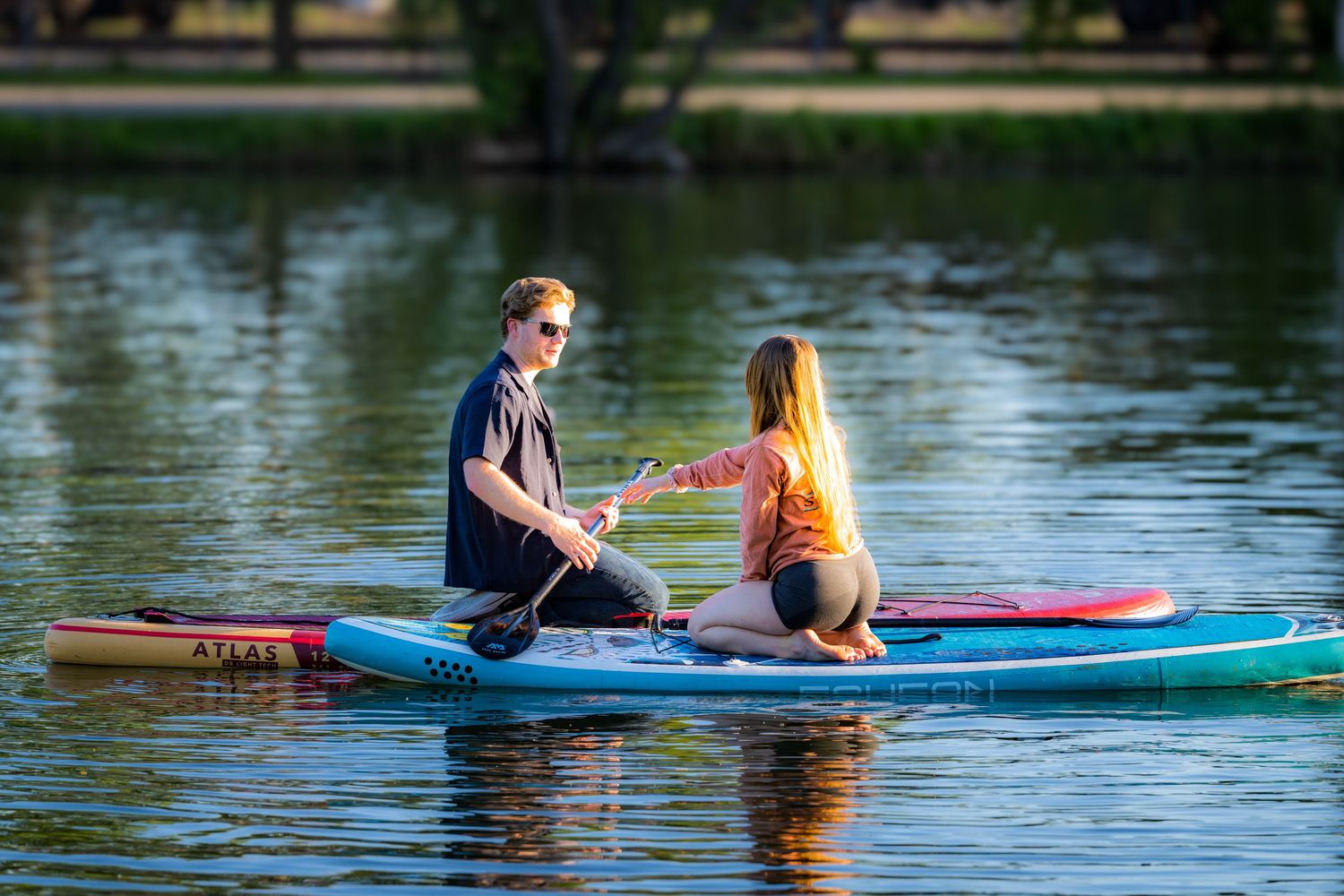 Couple sitting together on a paddleboard on a calm lake sharing a romantic moment.