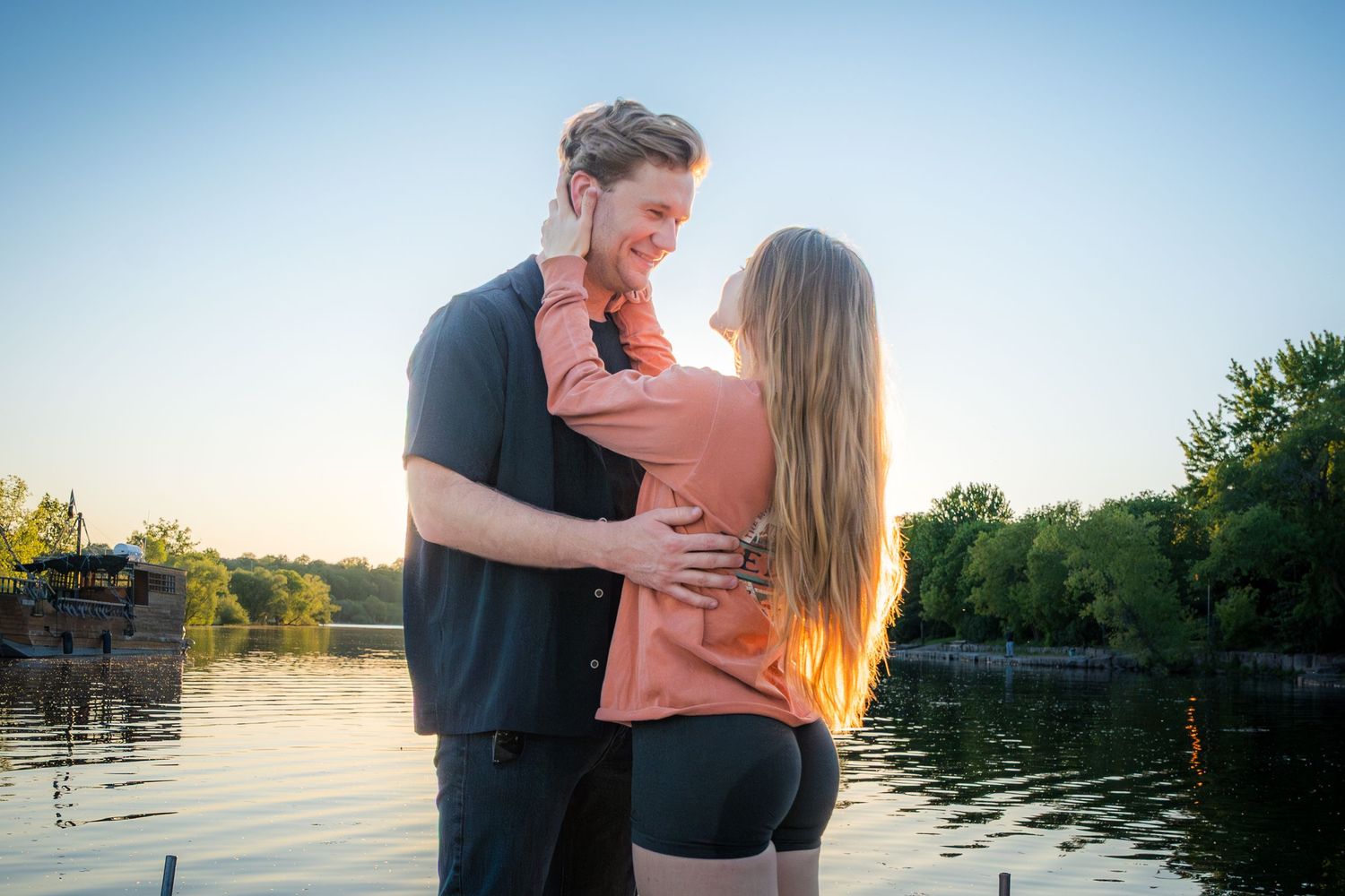 Romantic couple embracing near a lake at sunset, sharing a tender moment outdoors.