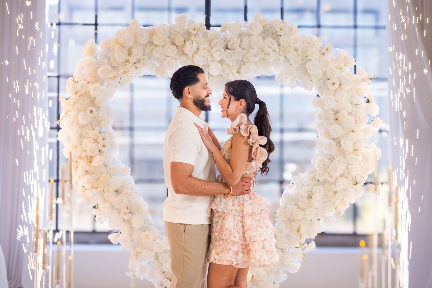 Couple sharing a romantic moment standing inside a heart-shaped white floral arch with sparklers.