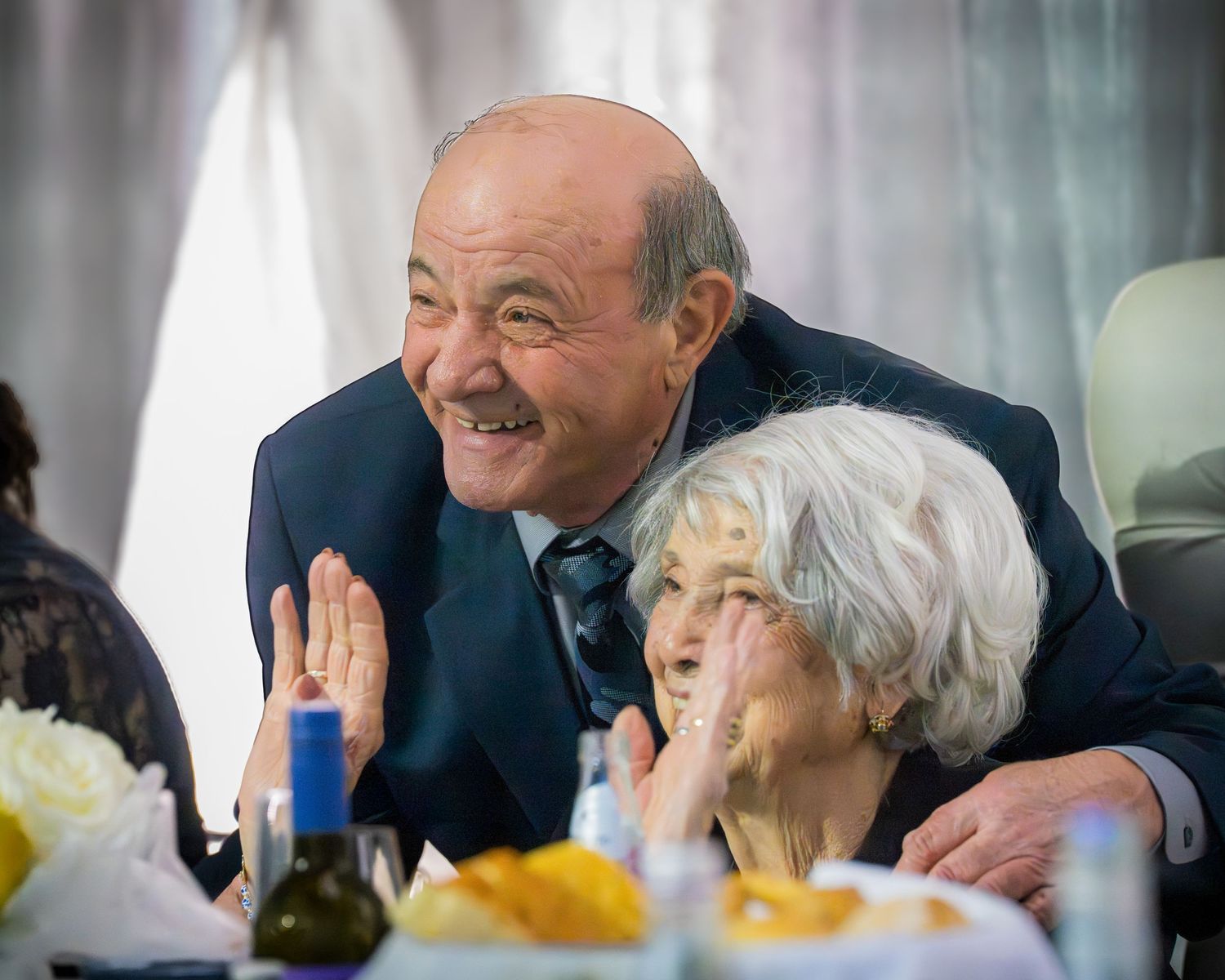 Cheerful elderly couple laughing and embracing together at a festive formal banquet celebration.